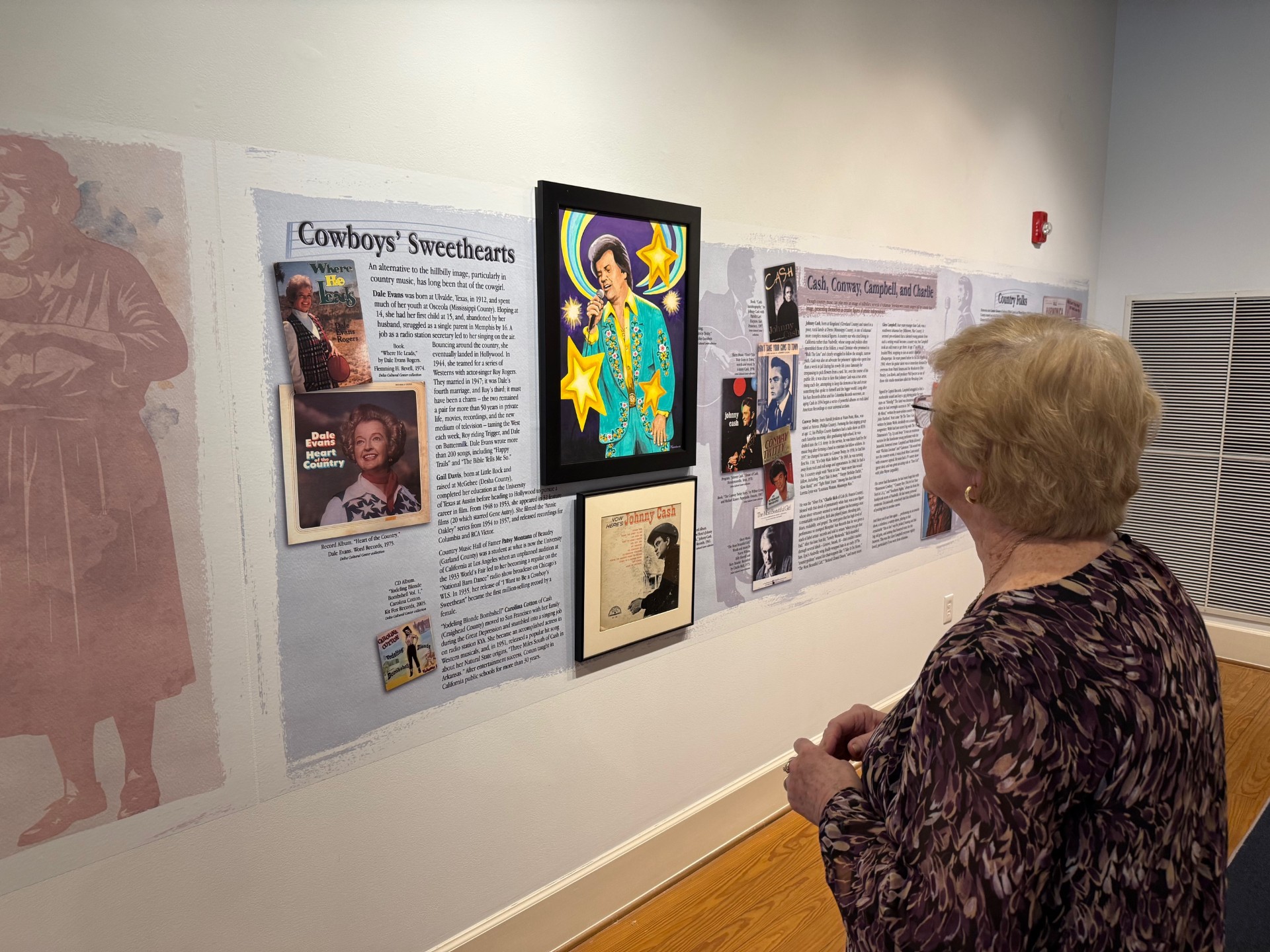 An older woman looking at text and images on a gallery wall.