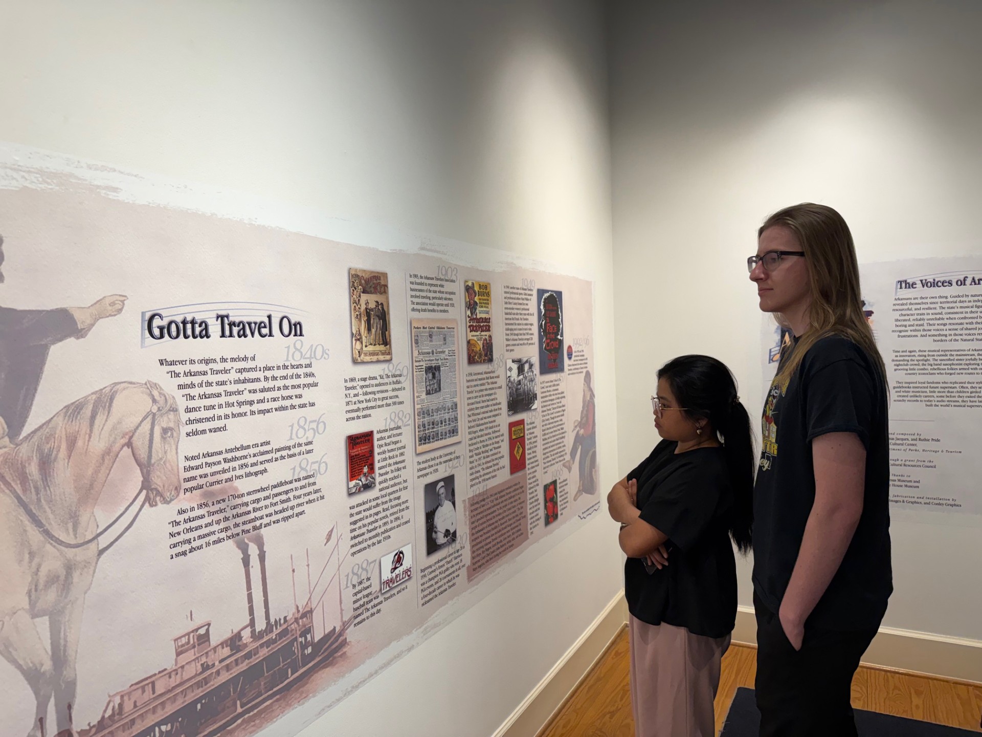 An adult and a child looking at text and images on a gallery wall.