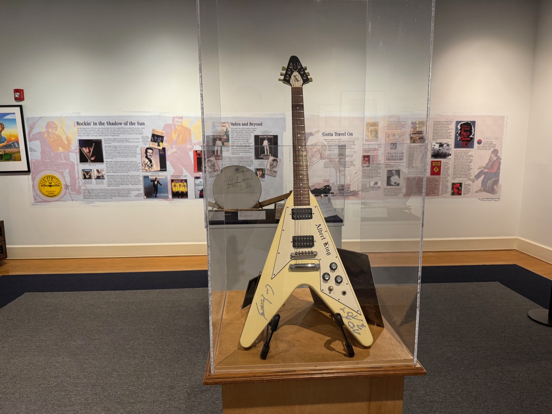 A small cream colored guitar in a display case in a museum.