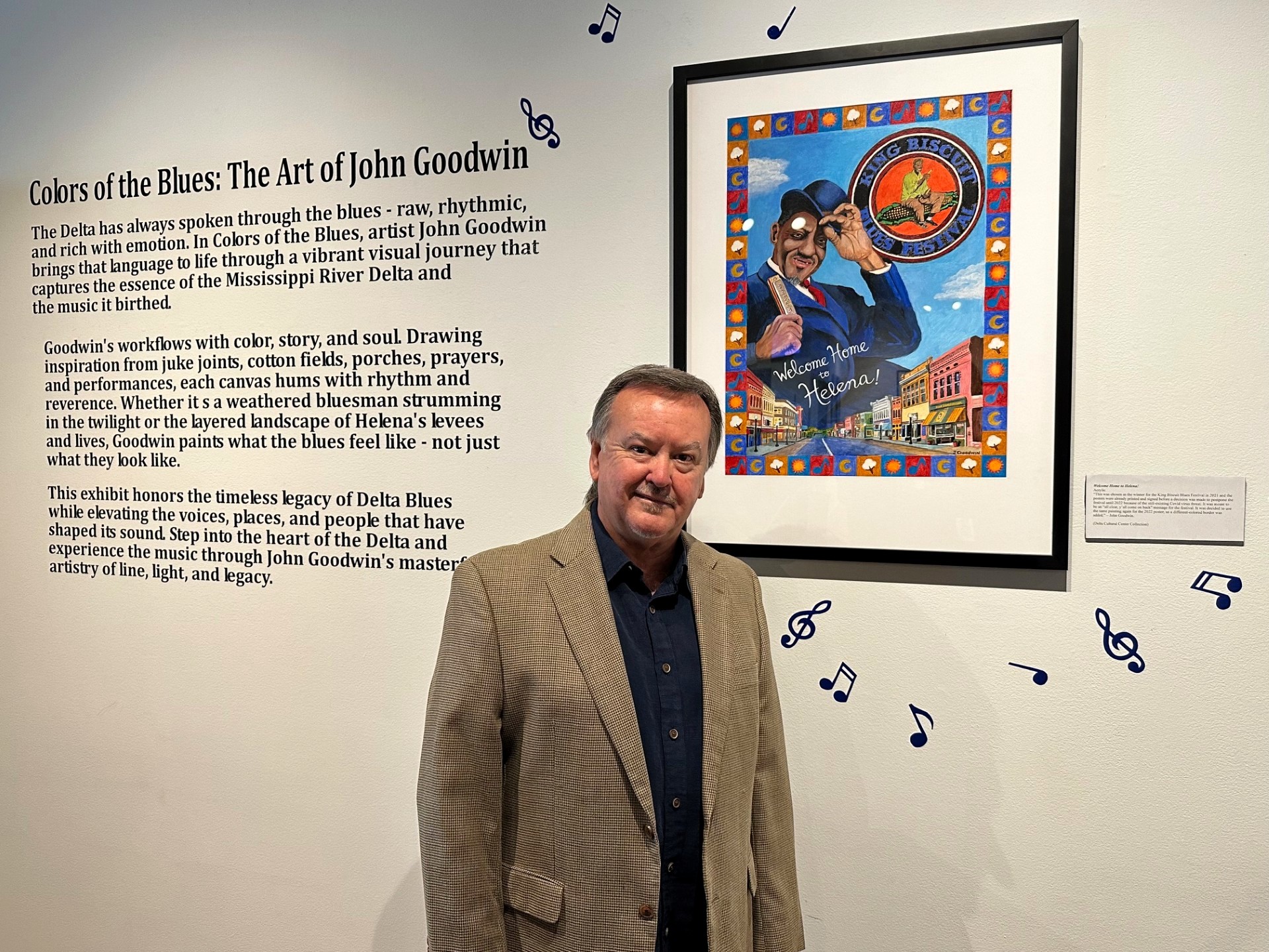 Artist John Goodwin in a brown suit jacket standing in front of his new Exhibit.