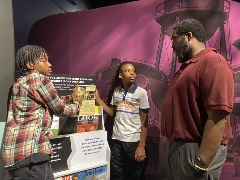 Twoboysandamaninteractwithamockmagazinedisplay