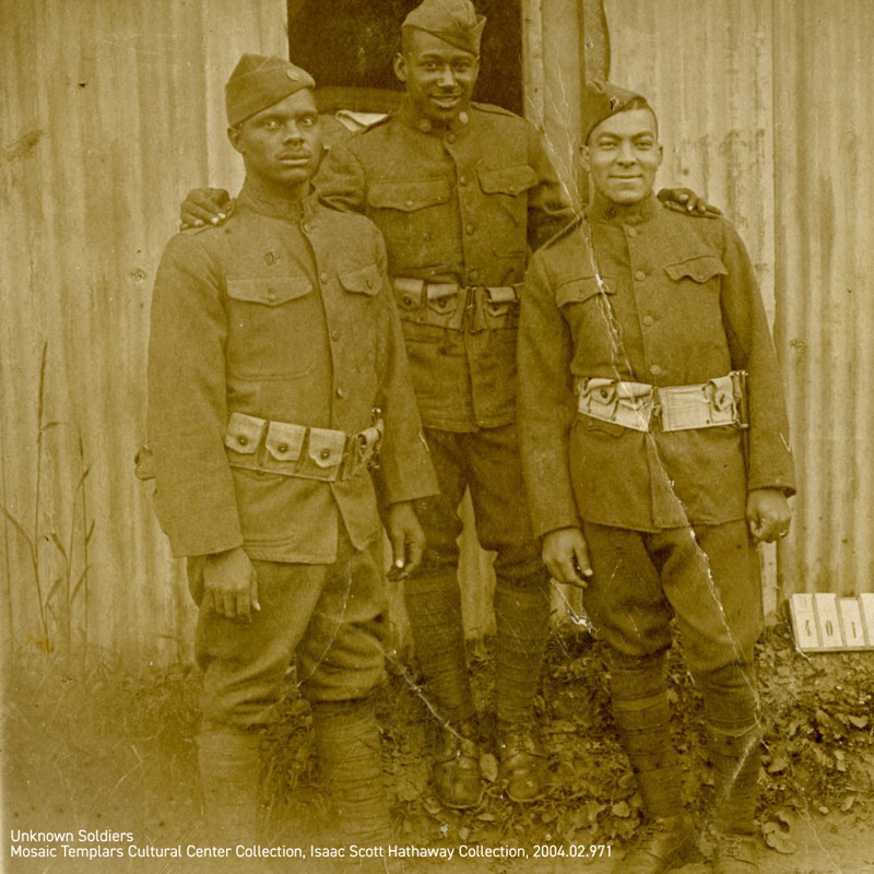 Three African American soldiers posing together in front of a metal wall side by side.