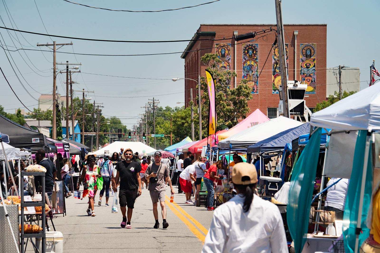 People walk between booths of vendors selling various items and food.