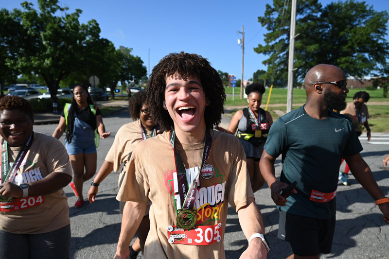 A young man walks with a group of people wearing a medal and smiling.