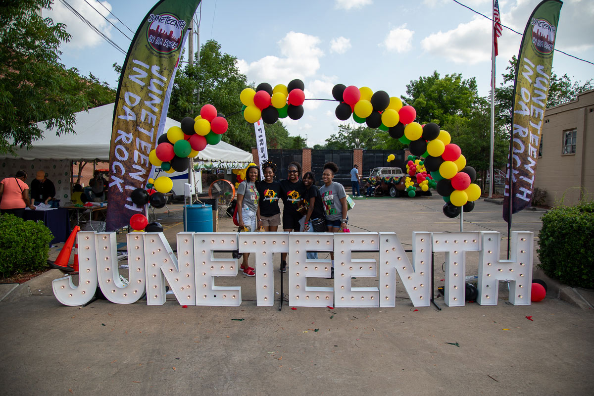 Five ladies pose together behind a large Junteenth sign under a balloon arch.
