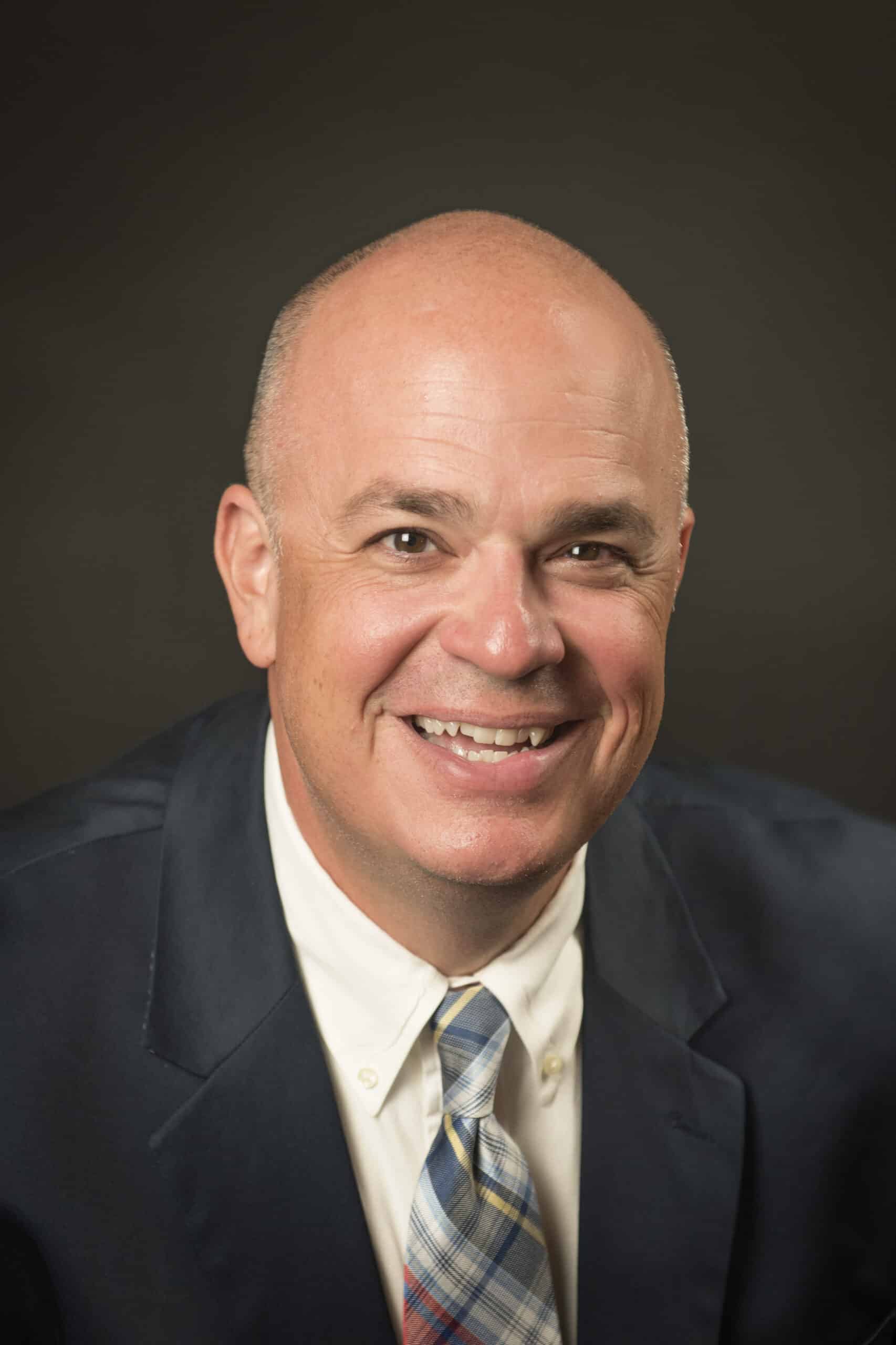 Shea Lewis, a man in a dark suit with a patterned tie smiling.