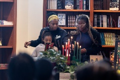 Two Black women and a girl light the Kinara for Kwanzaa
